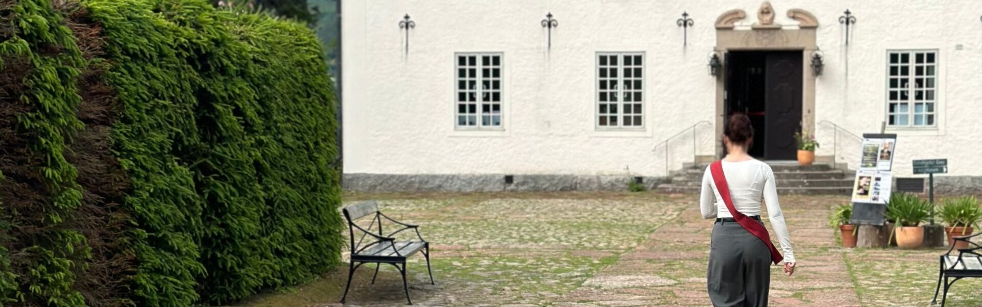 En guide går längs borggården mot Hildasholms entré, omgiven av grönska.