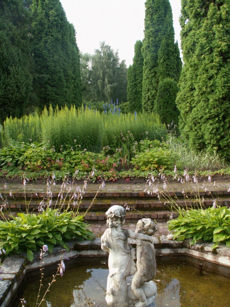 En skulptur av två lekande barn står i en liten damm omgiven av grönska.